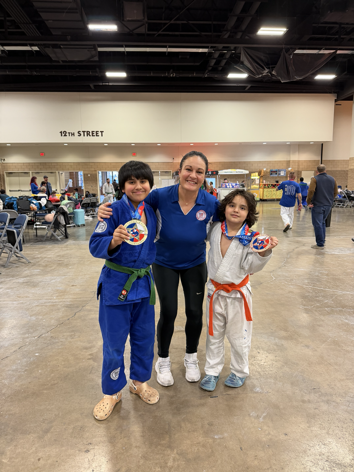 Sensei Carrie Chandler with two young athletes proudly holding their competition medals