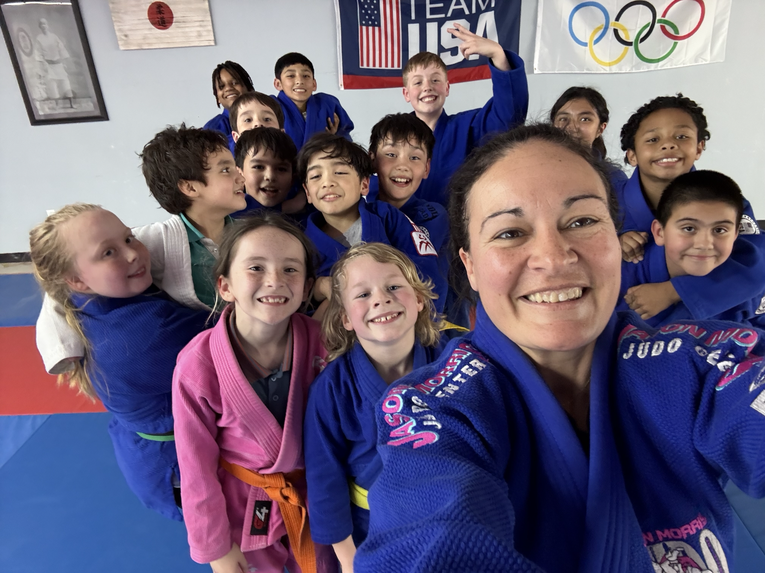 Sensei Carrie with a group of happy kids in judo uniforms inside the dojo